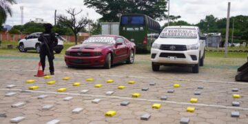 Un agente policial resguarda la droga y los vehículos incautados.