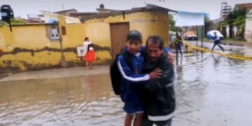 Un estudiante es llevado en brazos por la inundación en un colegio de Cochabamba.