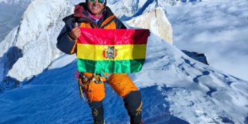 Hugo Ayaviri en la cima de la montaña, con la bandera de Bolivia.