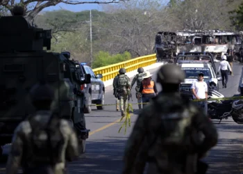 Operativo de seguridad en México tras la muerte del líder del CJNG, con fuerzas federales resguardando un puente y un autobús incendiado al fondo.