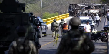 Operativo de seguridad en México tras la muerte del líder del CJNG, con fuerzas federales resguardando un puente y un autobús incendiado al fondo.